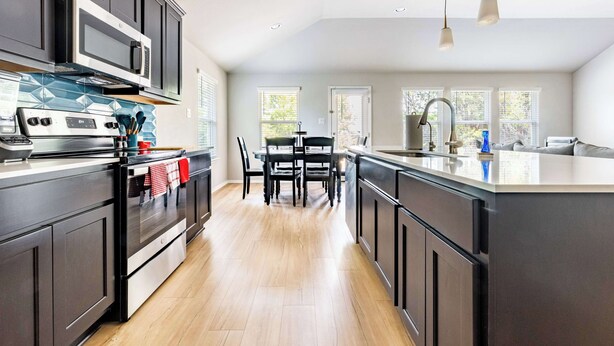 Une cuisine moderne avec des meubles de couleur sombre, un îlot central, un coin repas avec des chaises et une vue par les fenêtres.