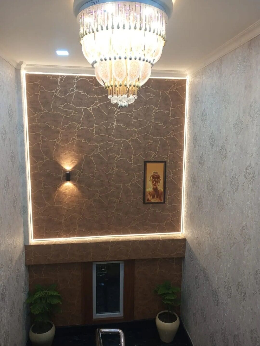 Una habitación con una araña, una lámpara de pared, una estatua de Buda enmarco y dos plantas en macetas.