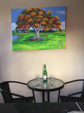 A painting of a tree on a wall, a table with two glasses and a bottle, and two chairs. - Higuey Center City, Leslie's Villa (Higuey)