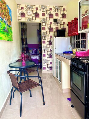 A compact kitchen with a refrigerator, stove, and sink. There is a dining area with a table and chairs. - Higuey Center City, Leslie's Villa (Higuey)