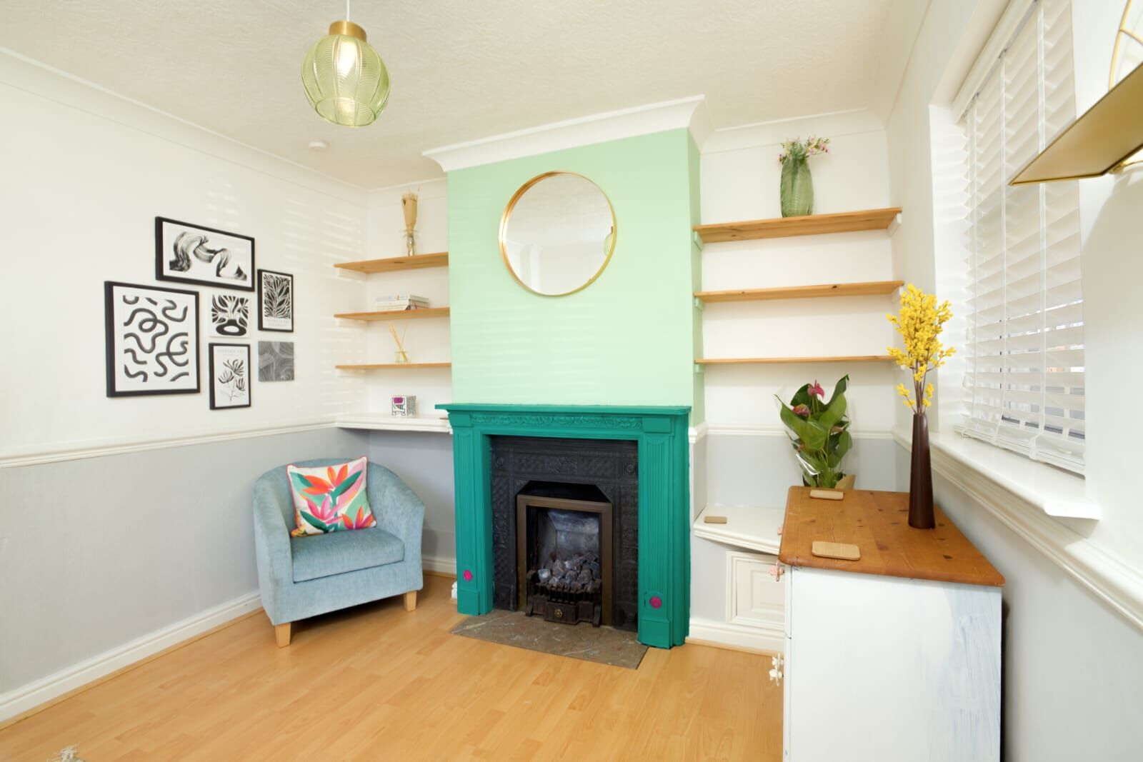 A living room with a fireplace, a blue armchair, and wall-mounted shelves.