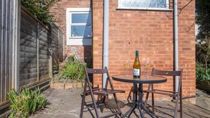 Une terrasse extérieure avec une table ronde et quatre chaises, une bouteille de vin et deux verres posés sur la table.