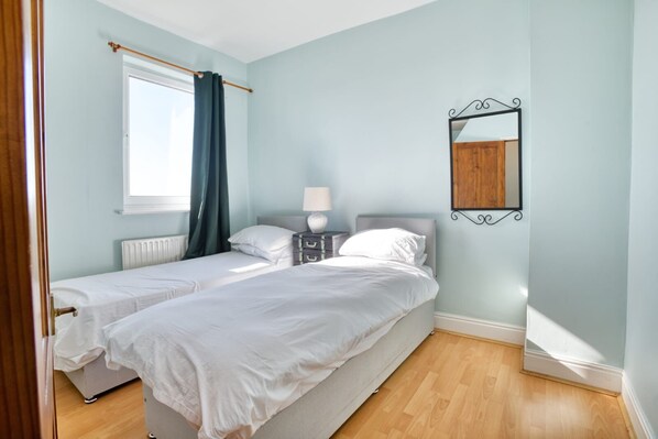A bedroom with two beds, a window with curtains, a bedside table with a lamp, and a mirror on the wall. - Lincoln Gem: Between Cathedral & City - Pass the Keys (Lincoln)