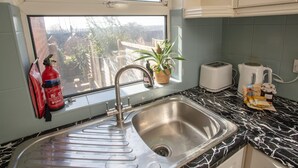 Une cuisine équipée d’un évier en acier inoxydable, d’une fenêtre donnant sur des immeubles et des arbres, d’un extincteur, d’un grille-pain et d’une bouilloire.