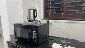 A kitchen with a microwave, a kettle, and a pizza oven on a black countertop. - Nisarg Homestay with Kitchen (Bhuj)
