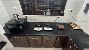 A kitchen with a microwave, two induction cooktops, a kettle, and a coffee maker on the counter. - Nisarg Homestay with Kitchen (Bhuj)