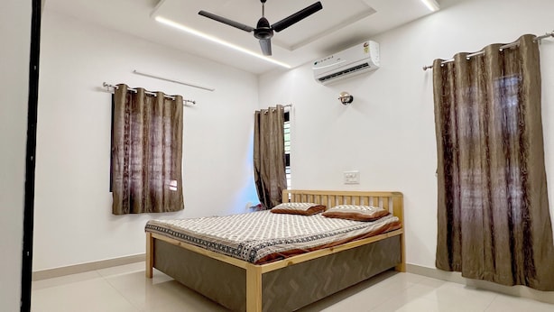 A bedroom with a bed, ceiling fan, air conditioning unit, and curtains. - Nisarg Homestay with Kitchen (Bhuj)