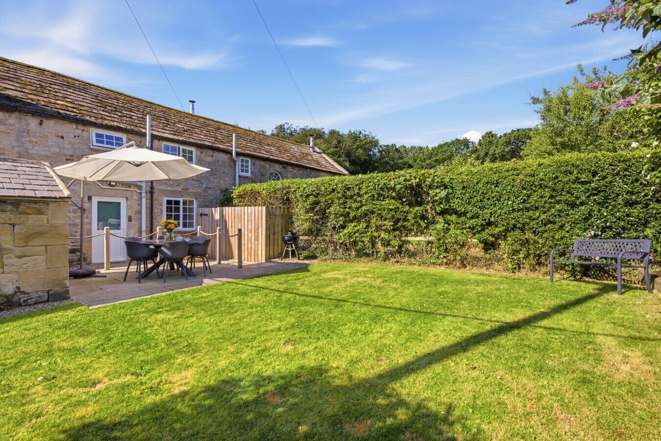 A stone house with a patio, a table with chairs, and a hedge in the backyard.