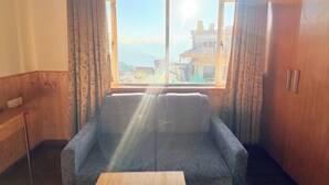 Een kamer met een bank, een houten tafel en een raam met uitzicht op gebouwen en bergen.