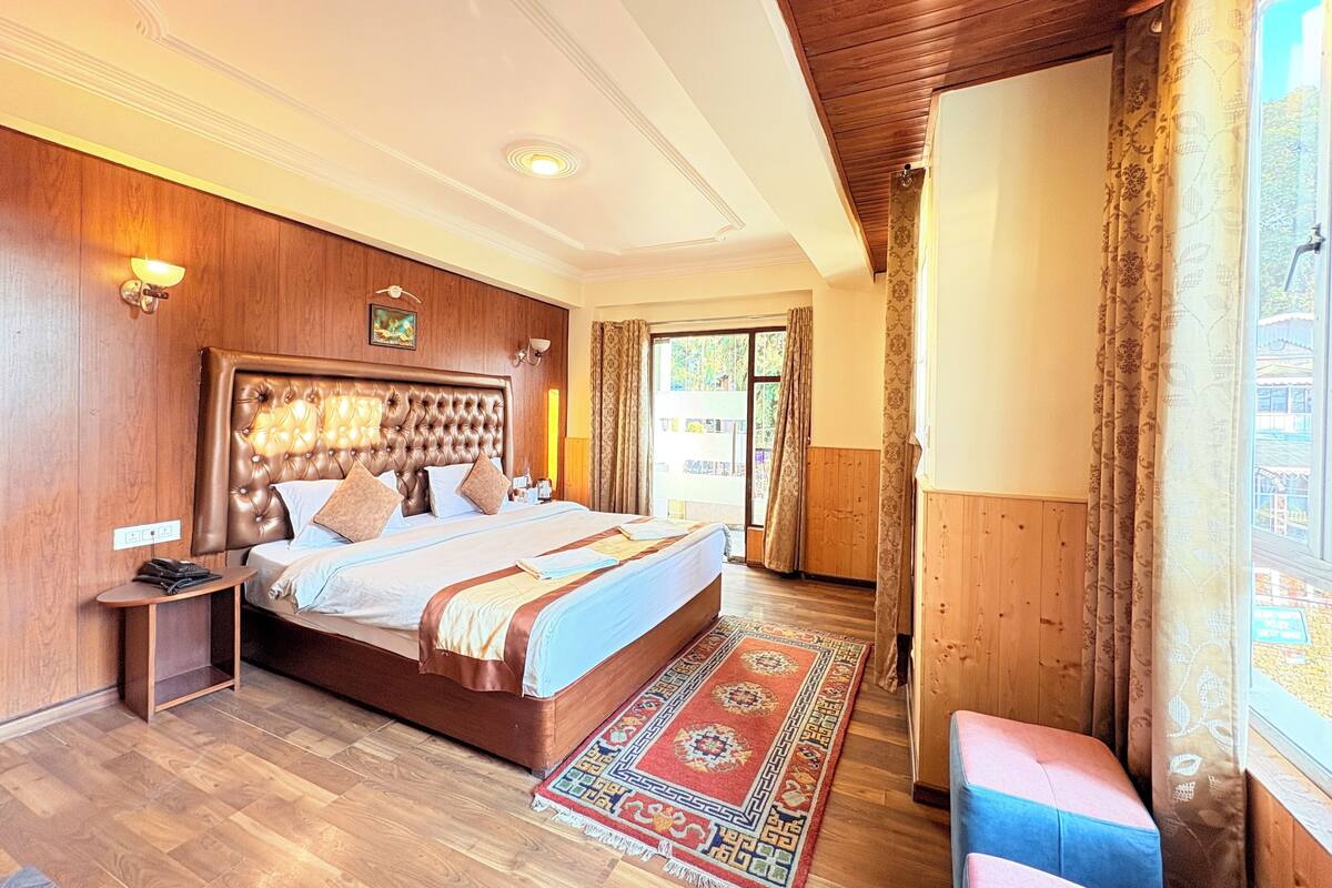 Un dormitorio con una cama grande, paneles de madera, una mesita de noche, un banco y vistas a través de una ventana.