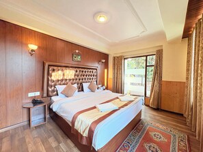 Une chambre d’hôtel avec un grand lit, des boiseries, une table de chevet, une fenêtre avec des rideaux et une vue sur la verdure.