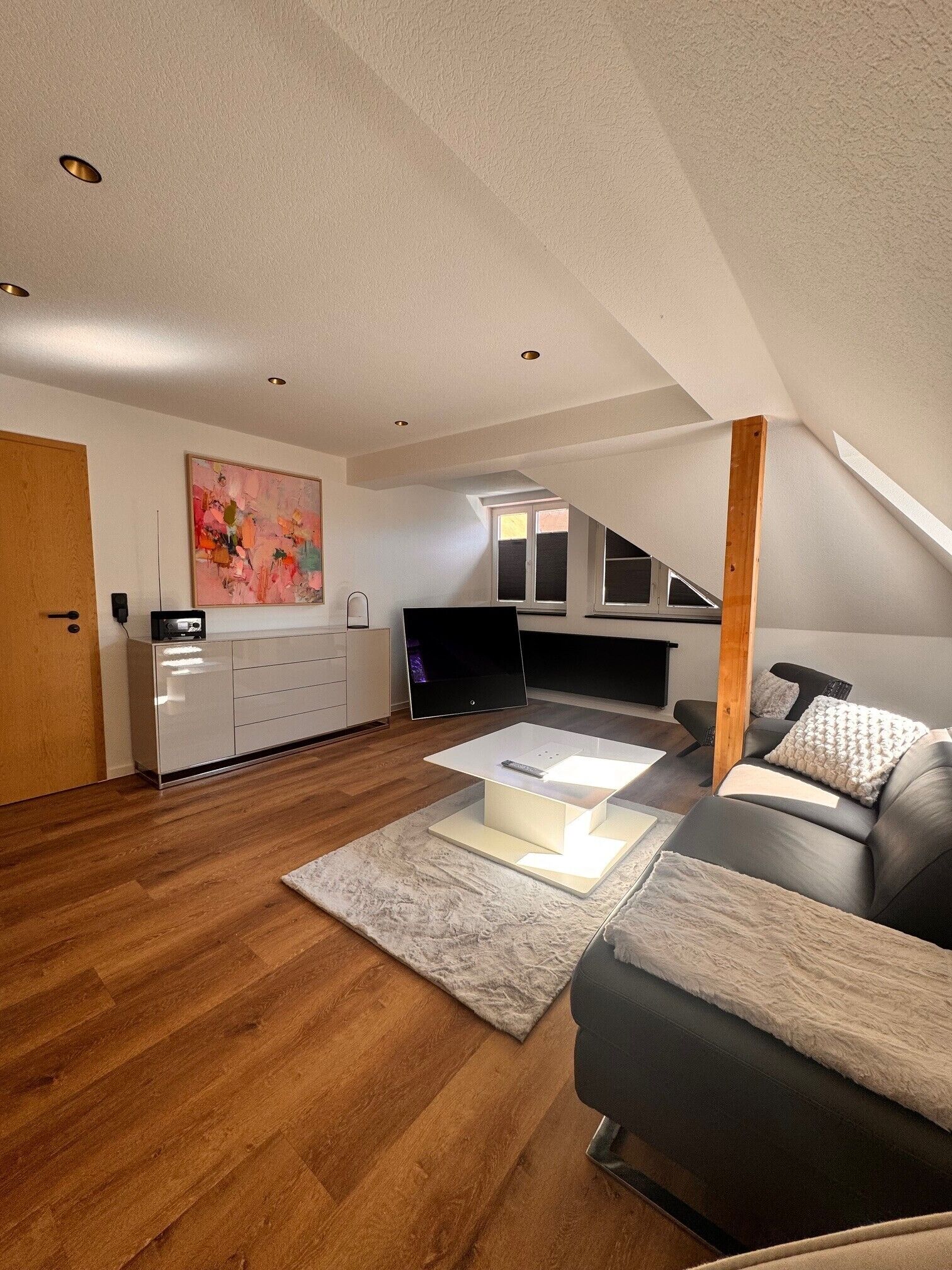 Un espace de vie moderne avec un plancher en bois, un canapé blanc, une table basse et un tableau accroché au mur.