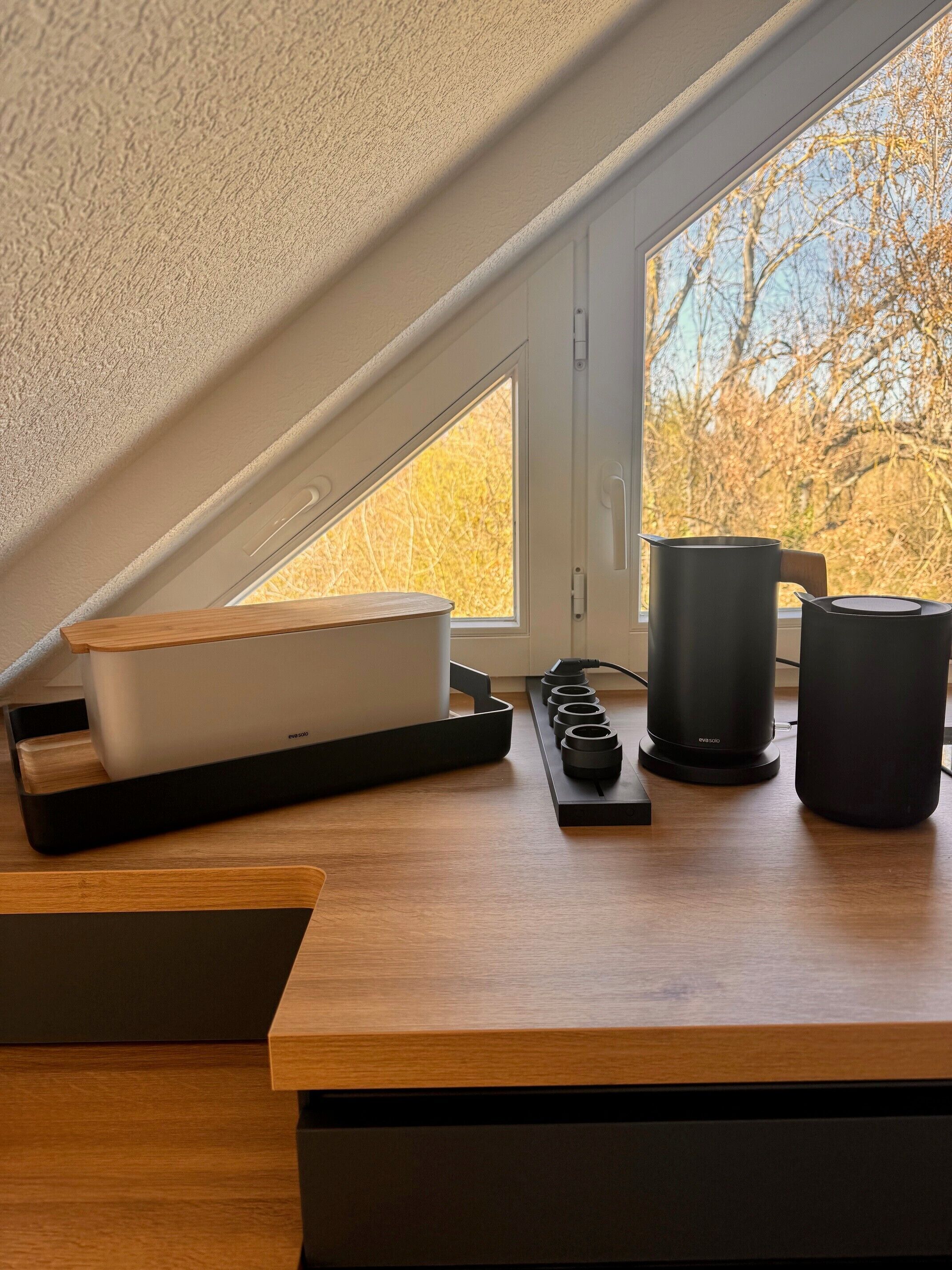 A modern kitchen with a wooden countertop, a coffee maker, a kettle, and a power strip.