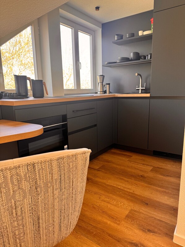 A modern kitchen with a wooden countertop, a sink, and a window with a view of trees.