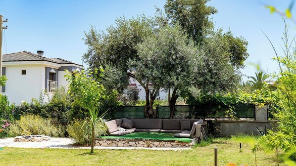 Un jardín con un hogar de piedra, césped verde y un sofá exterior negro.