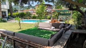 A poolside area with a sofa and a cat, surrounded by greenery and a view of buildings. - 6 Rooms Stone Villa With Private Pool - Sea and Mountain Views (Kemer)