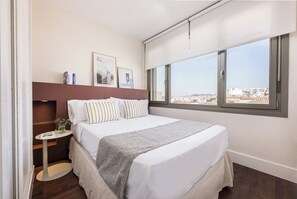 A hotel room with a large bed, a small side table, a window with a city view, and a headboard. - Victoria XXIII - One Bedroom Apartment, Sleeps 2 (Malaga)