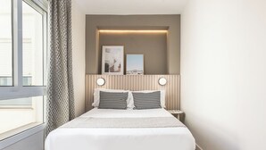 Una camera d'albergo ordinata con un letto grande, un comodino, tende e una finestra con tende.