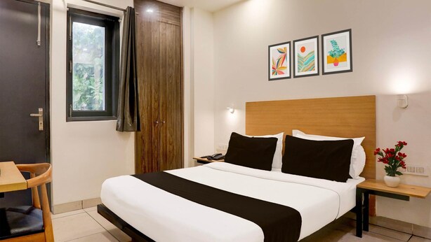 Een hotelkamer met een bed, een bureau, een stoel, een nachtkastje, een wandlamp en een raam met gordijnen.