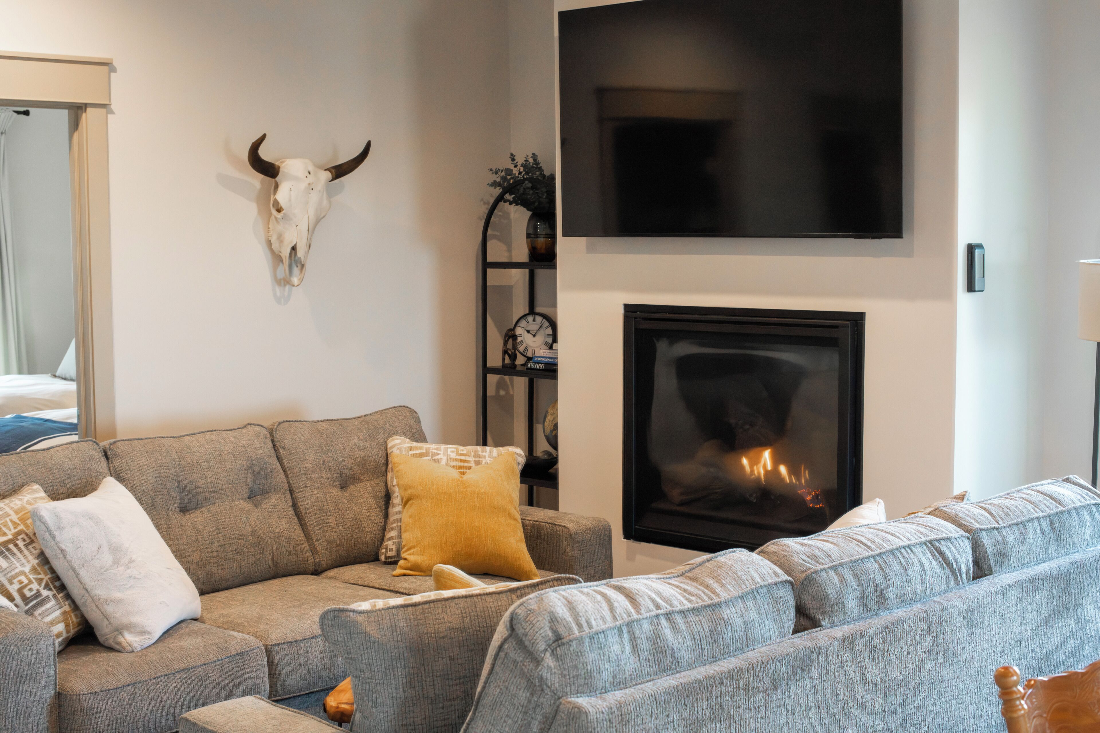 A living room with a sofa, a fireplace, a mounted TV, and a bull skull decoration.