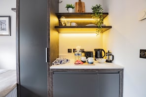 A compact kitchenette with a countertop, a coffee maker, a kettle, a bowl, and a towel.