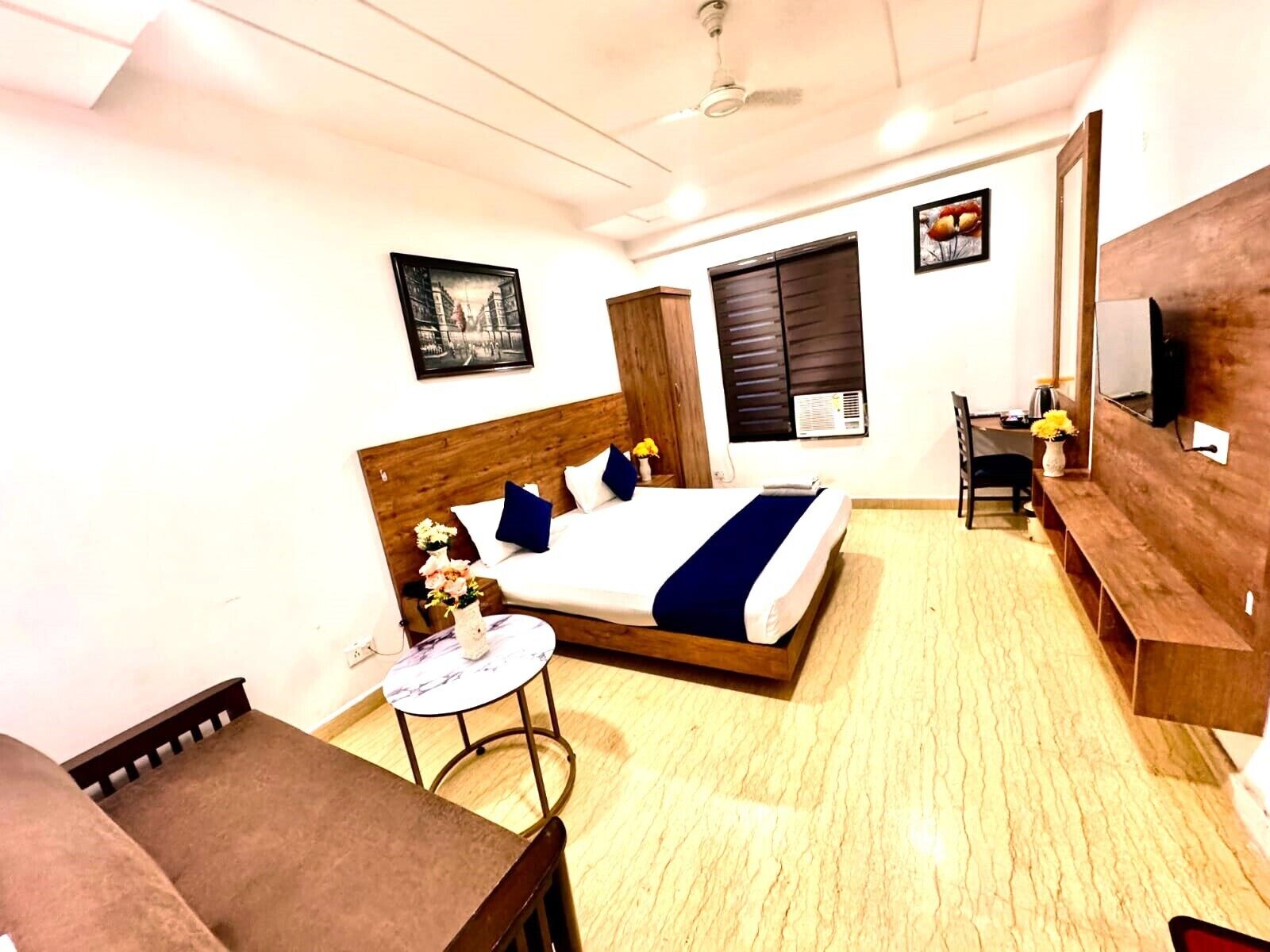 A hotel room with a bed, a small round table, a chair, a desk, and a TV.