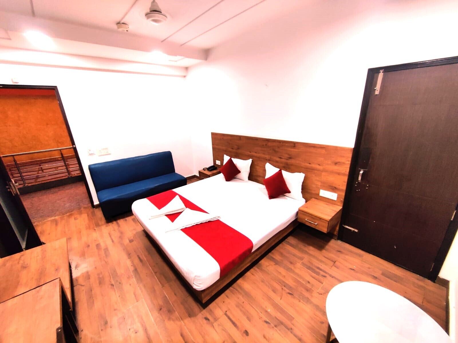 A bedroom with a wooden bed, a blue sofa, a wooden nightstand, and a wooden door.