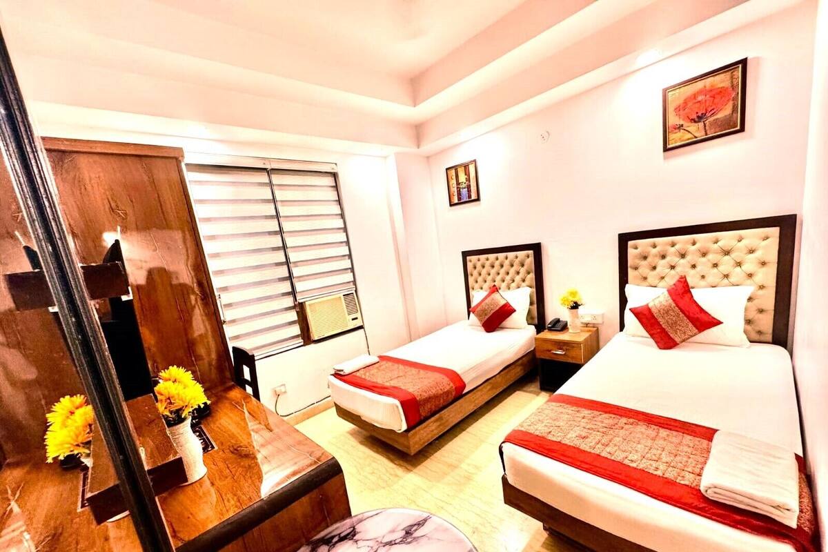 A hotel room with two beds, a wooden desk, a marble table, a mirror, and a window with blinds.