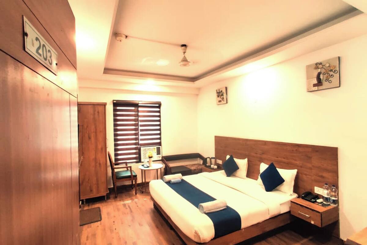 A hotel room with a bed, bedside table, nightstand, and a desk with a chair.