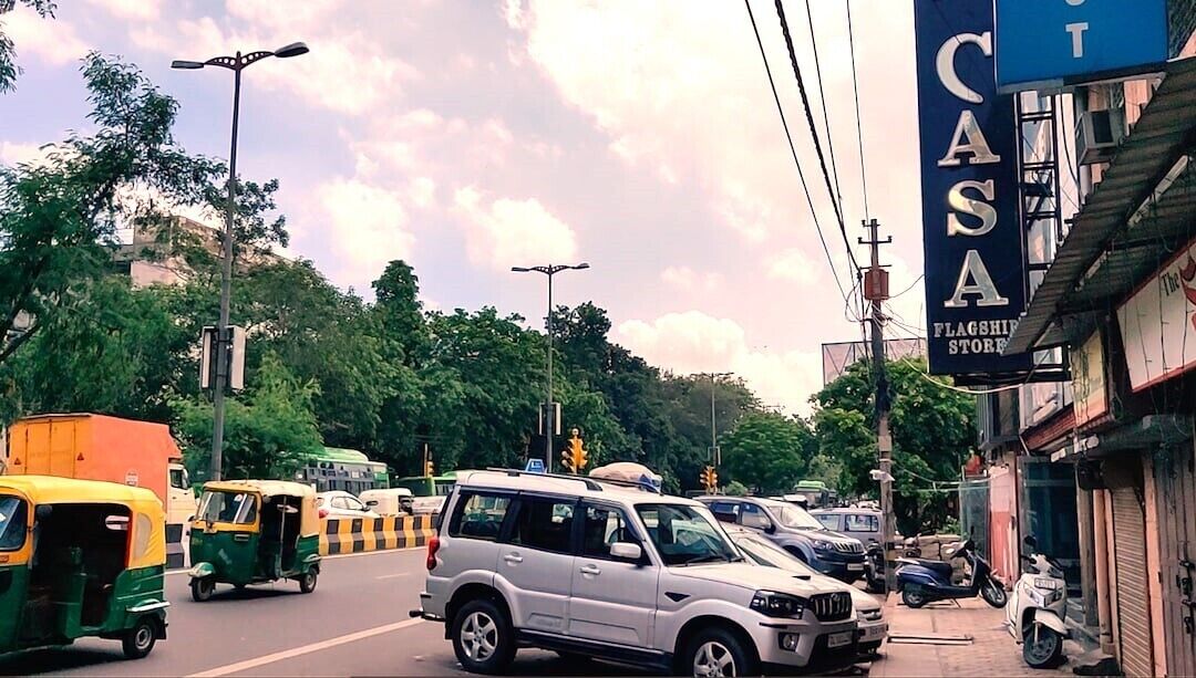 Escena callejera con un SUV blanco, tuk-tuks y un edificio con un letrero que dice 'CASA FLAGSHIP STORE'.