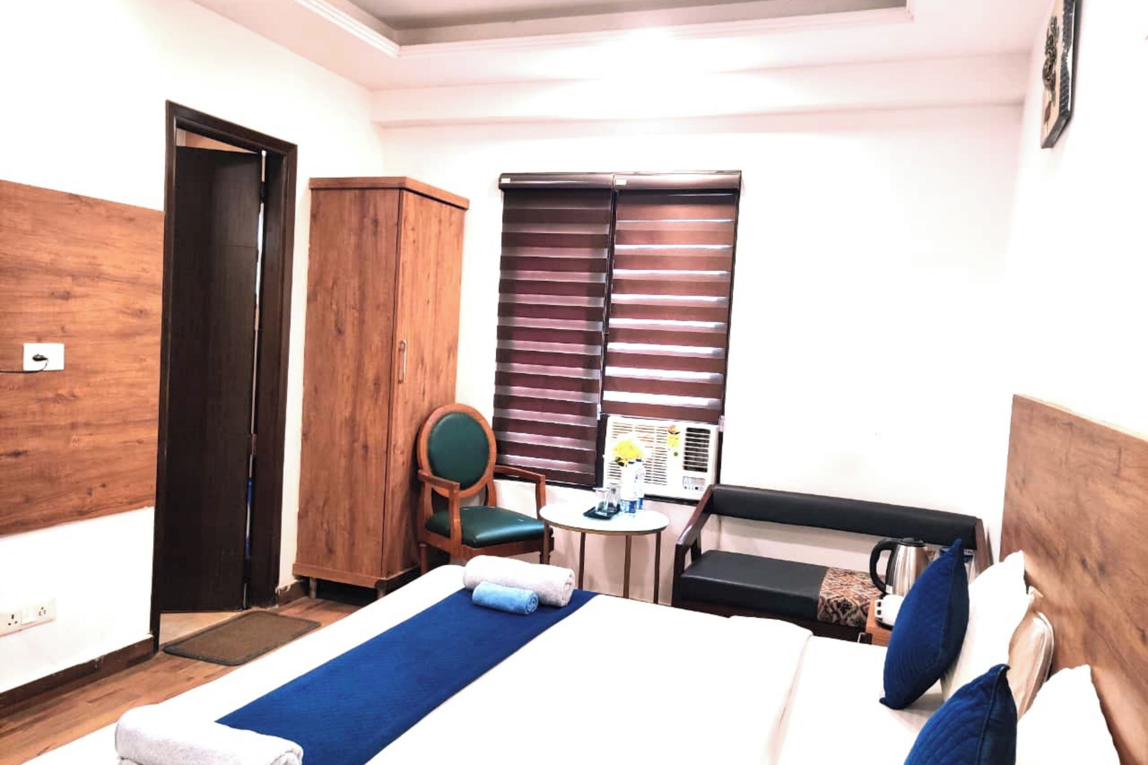 Quarto de hotel com cama, escrivaninha com cadeira, guarda-roupa e janela com persianas.