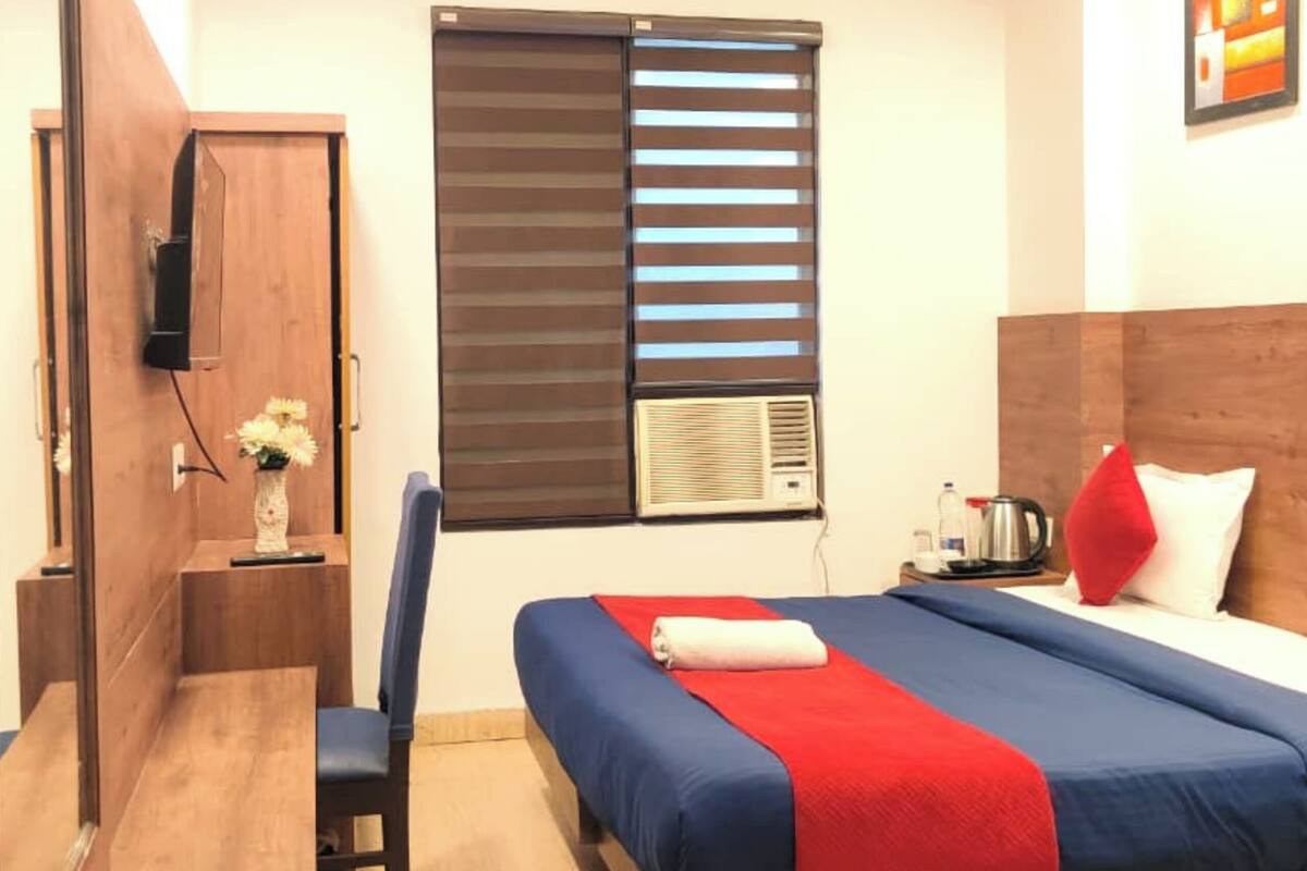 A hotel room with two beds, a desk, a chair, a TV, and a window with blinds.