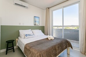 A hotel room with a bed, a window, a curtain, a picture on the wall, and a small stool. - Beautiful view | in the heart of Campeche (Florianópolis)