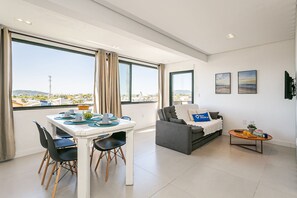A modern living room with a dining area, large windows, and a view of the cityscape. - Beautiful view | in the heart of Campeche (Florianópolis)