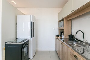 A compact kitchen with a gas stove, oven, refrigerator, and a sink with a wooden countertop. - Beautiful view | in the heart of Campeche (Florianópolis)