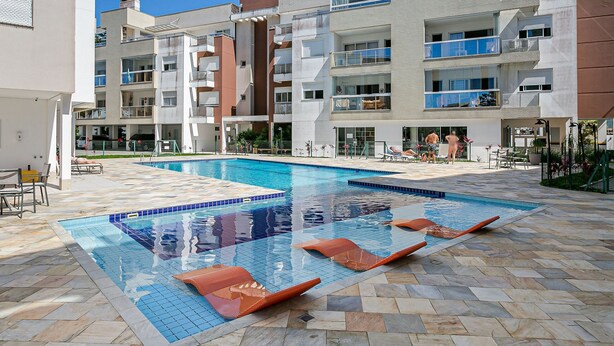 Ein Schwimmbecken mit Liegestühlen, einer gefliesten Terrasse und einem mehrstöckigen Gebäude mit Balkonen.