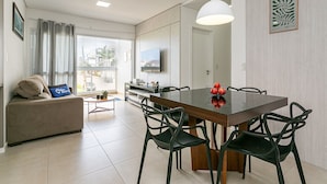 Ein modernes Wohnzimmer mit einer Couch, einem Esstisch, Stühlen, einem Fernseher und Blick durch ein großes Fenster.