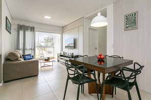 Un salon moderne comprenant un canapé, une table à manger, des chaises, un téléviseur et une vue dégagée sur l’extérieur grâce à une grande fenêtre.
