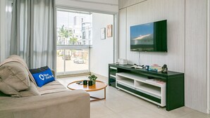 Ein modernes Wohnzimmer mit Sofa, Couchtisch, Fernseher und einer Schiebeglastür, die zu einem Außenbereich führt.