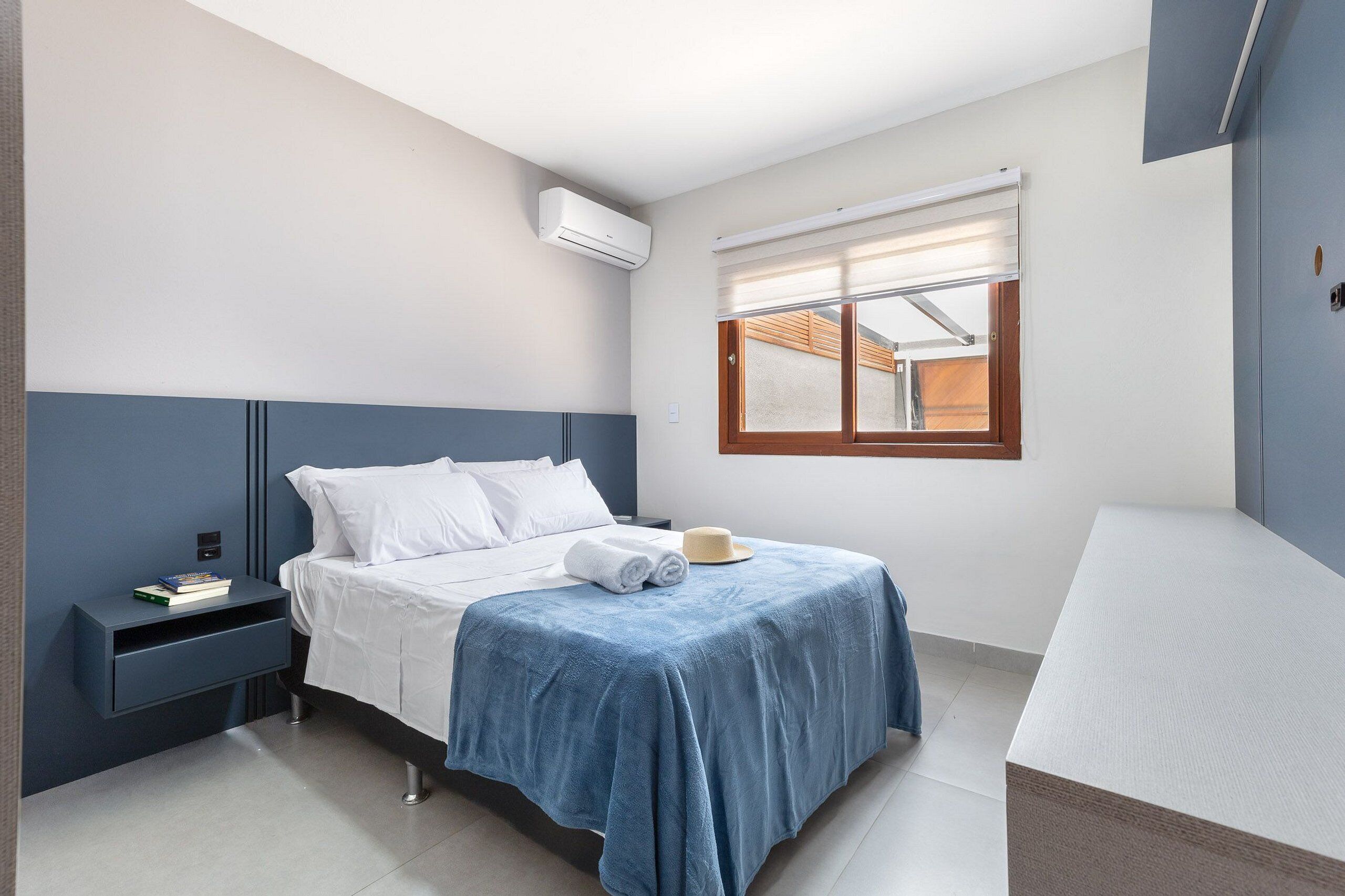 A bedroom with a bed, bedside table, and a window with blinds.