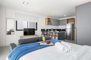 Een moderne hotelkamer met een bed, een televisie, een kitchenette en een eethoek.