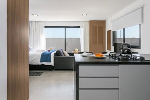 A modern hotel room with a bed, a small kitchenette, a dining area, and a large window. - Steps from the sea in Novo Campeche: high-end with pool (Florianópolis)