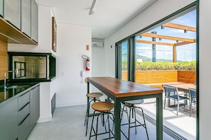 Een moderne keuken met een houten tafel en barstoelen, een brandblusser, en uitzicht op een houten terras met stoelen.