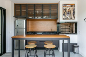 A modern kitchen with a central island, bar stools, a stainless steel refrigerator, and a wooden cabinet with glass doors. - Steps from the sea in Novo Campeche: high-end with pool (Florianópolis)