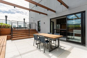 Une terrasse extérieure moderne, avec une table et des chaises en bois, un escalier et une porte vitrée donnant sur l’intérieur.