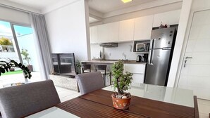 A modern kitchen with white cabinets, stainless steel appliances, and a dining area with a glass table and chairs. - Penthouse with jacuzzi near the sea Campeche (Florianópolis)