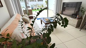 A modern living room with a sofa, a coffee table, a TV, and a large potted plant. - Penthouse with jacuzzi near the sea Campeche (Florianópolis)
