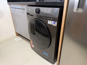 A modern, stainless steel front-loading washing machine with a digital display, a control panel, and a warranty sticker. - Pool and High Standard: very close to the beaches (Florianópolis)