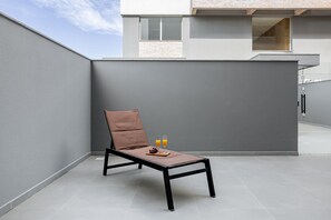 Ein moderner Loungesessel mit Tablett, zwei Orangensaftgläsern und Trauben auf einer Dachterrasse.