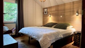 A bedroom with a bed, a window with curtains, a wall-mounted light, and a radiator. - Cozy Durbuy Chalet With Fireplace (Rendeux)